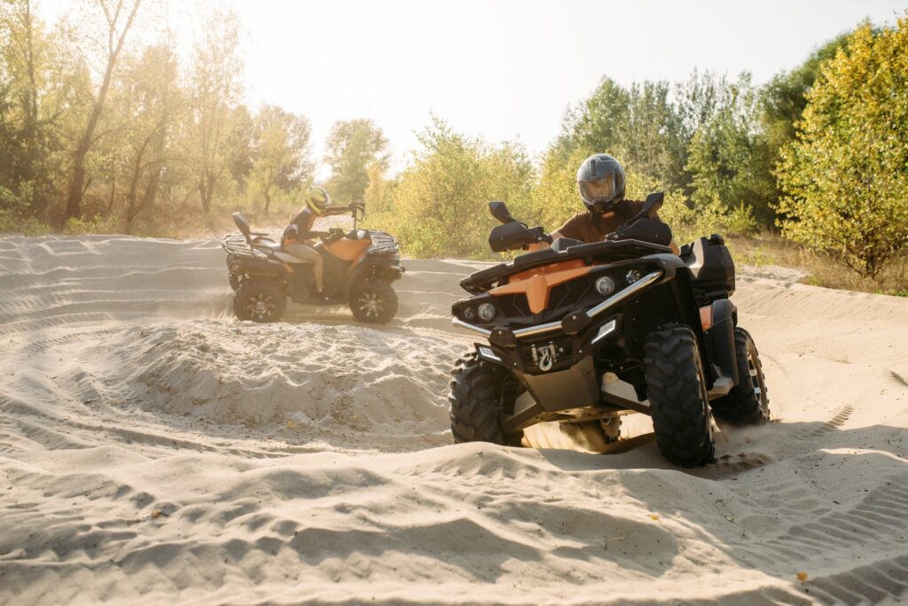 two atv riders in helmets ride in a circle on sand 1 e1645644912223.jpg
